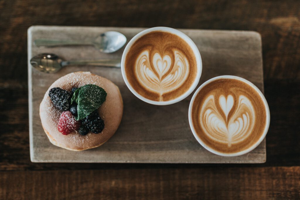 Zwei Cappuchino mit Latte Art und ein Donut mit frischen Früchten